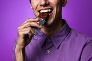 Pessoa comendo chocolate e feliz. Saúde bucal, cárie e mitos e verdades Imagem: Freepik